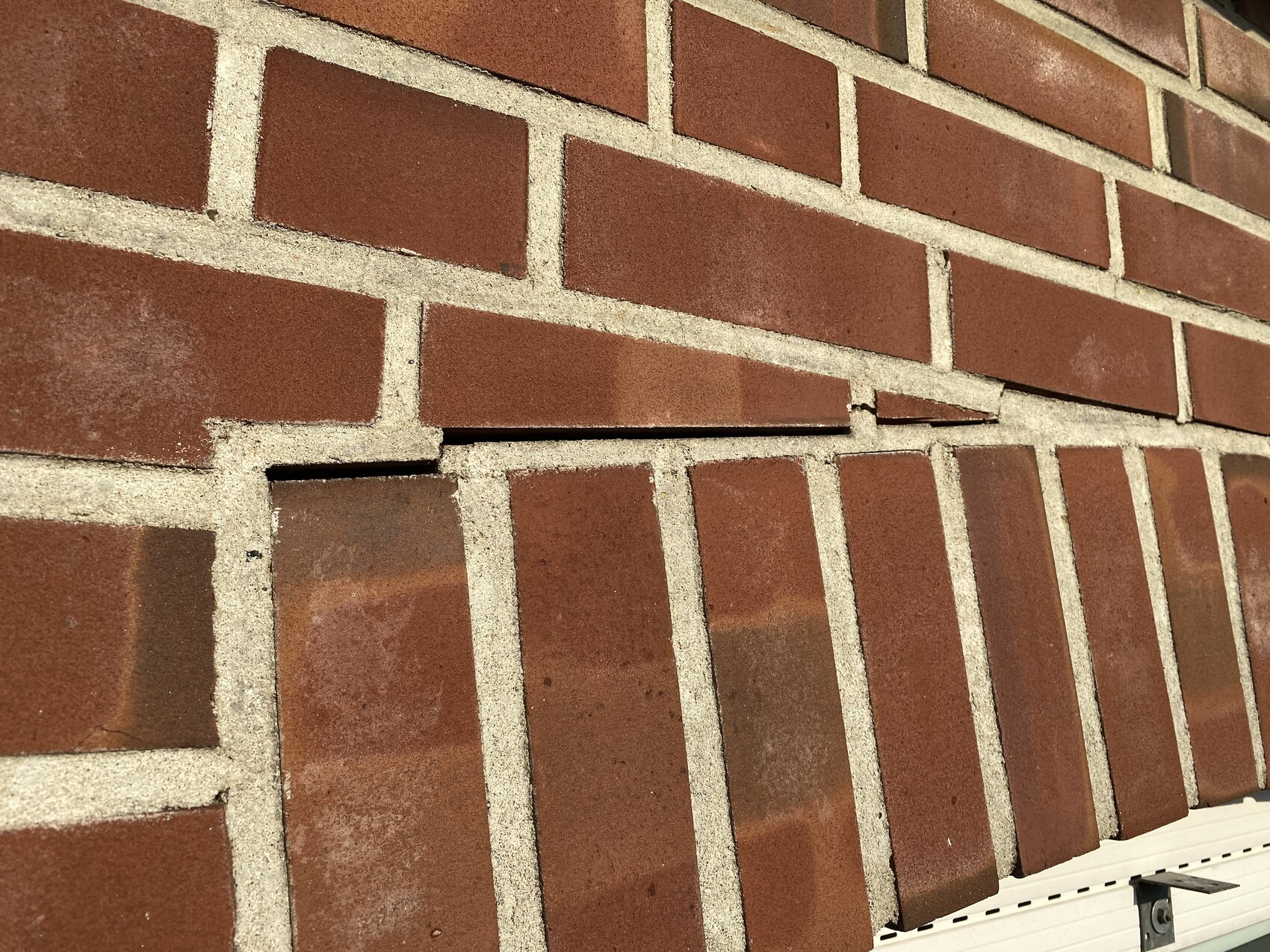 Rote Backsteinwand mit Beschädigung: ein Ziegel ragt schräg heraus, Mörtel sichtbar.