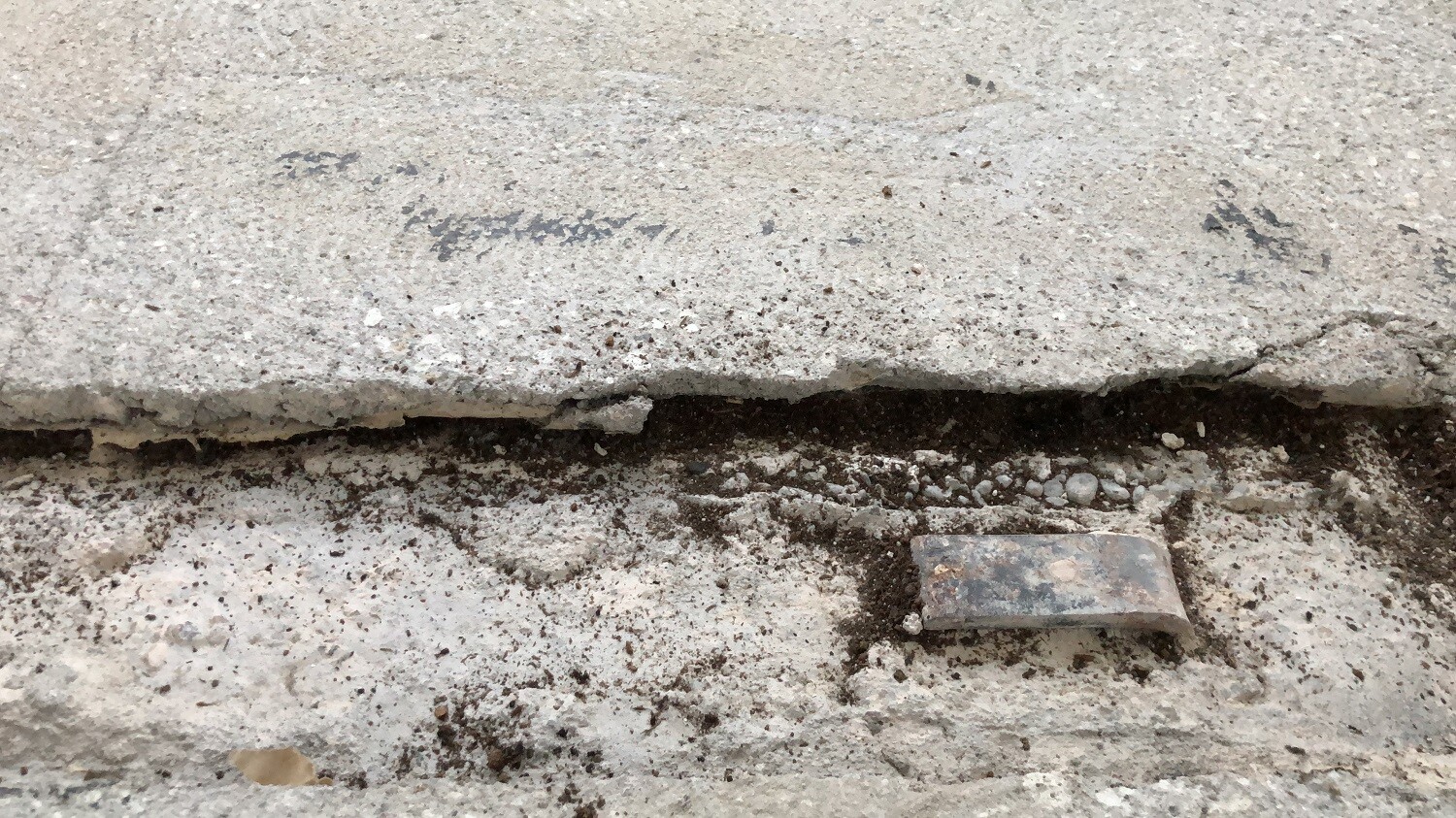 Nahaufnahme eines beschädigten Betonbodens mit Riss und rostigem Metallteil