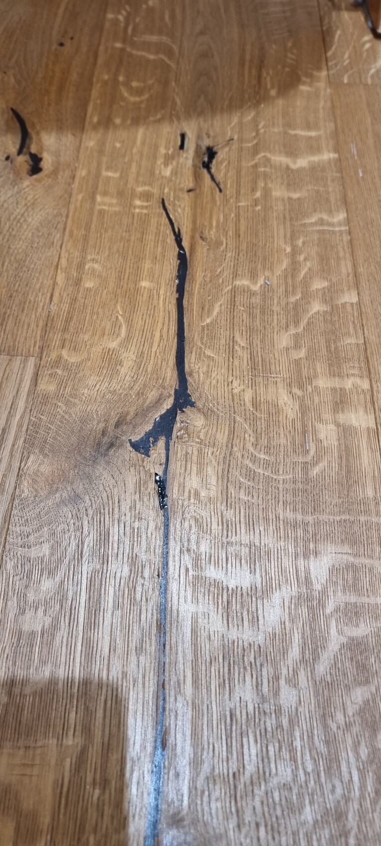 Holzfußboden mit einer langen Rissfuge und dunkler Kleberspur in der Fuge.