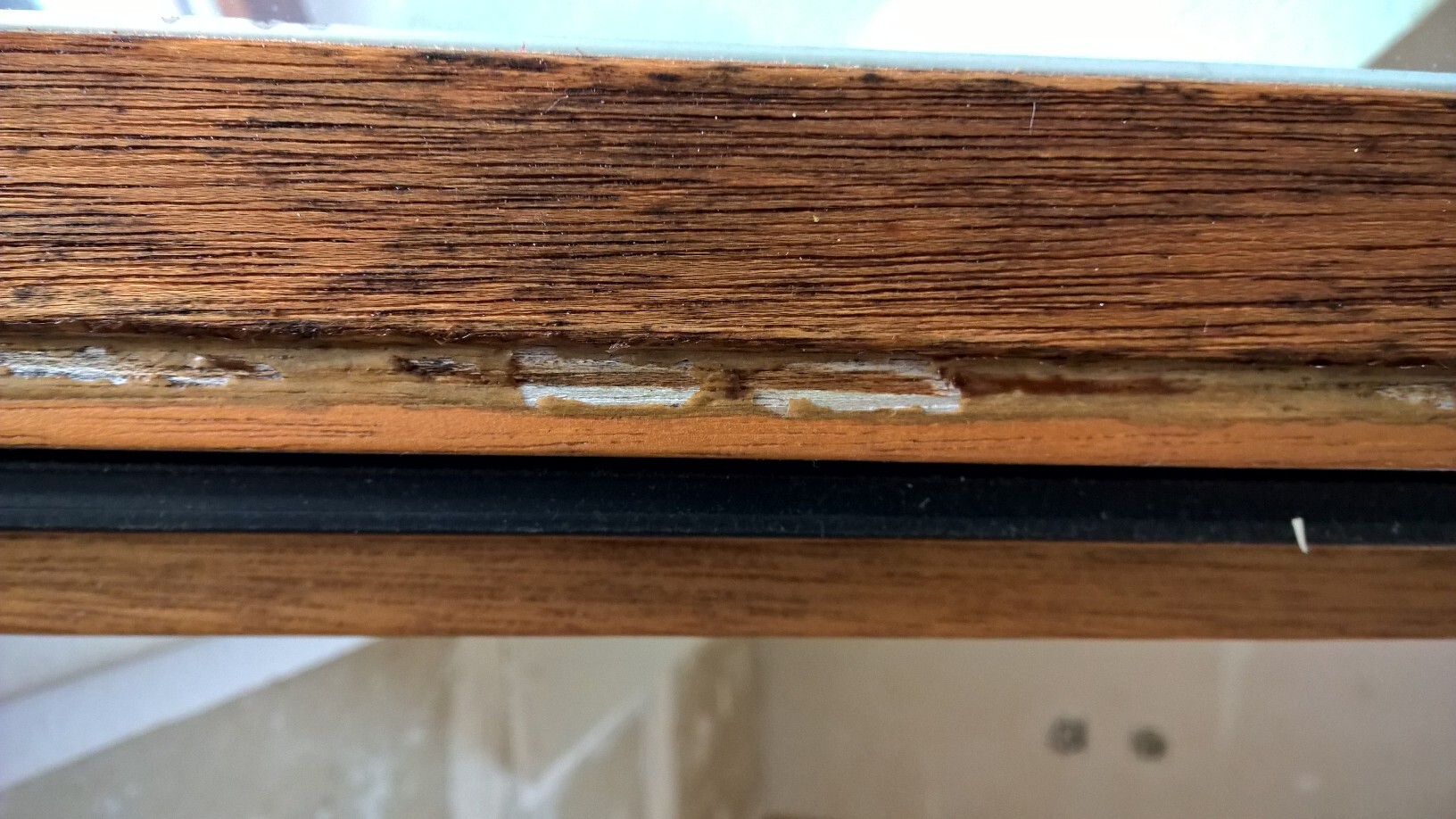 Nahaufnahme eines beschädigten Holzfensterrahmens mit abgeplatzter Oberfläche