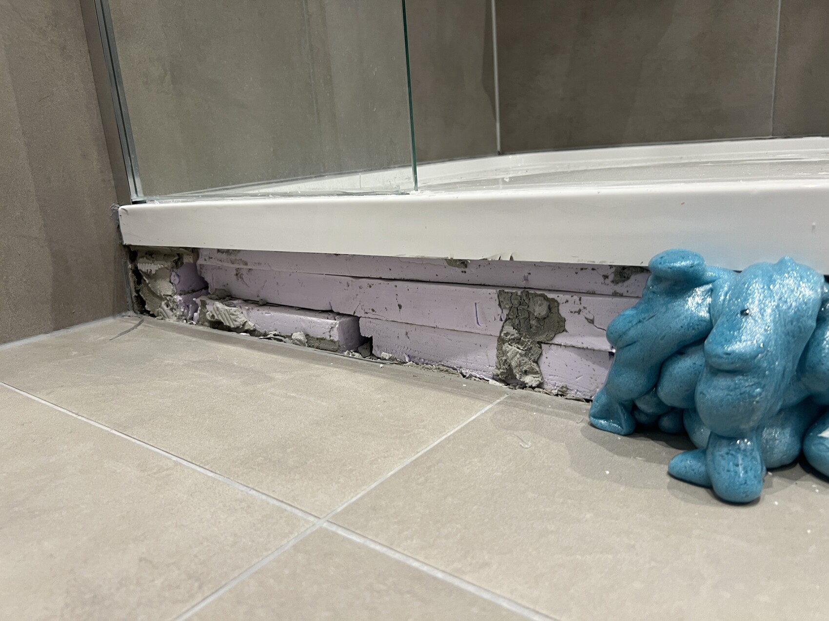 Dusche: beschädigter Unterrand mit lila Dämmplatten und blauem Schaumstoffklumpen.