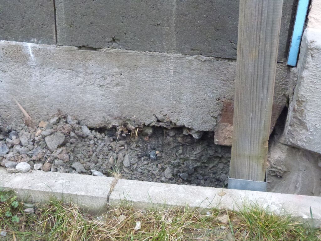 Beschädigter Fundamentbereich mit Erdreich, Betonwand und Holzpfosten