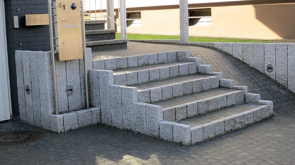 Graue Stein-Stufen mit seitlicher Rampe vor Gebäude; Briefkasten/Sprechanlage daneben.