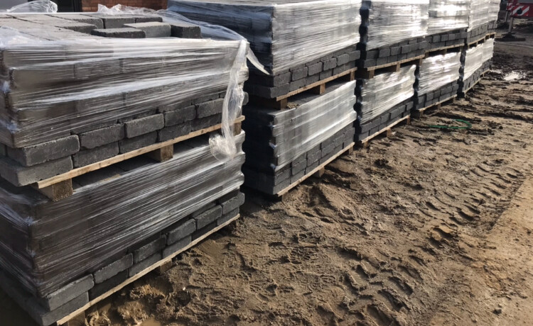 Stapel Betonpflastersteine auf Holzpaletten, verpackt mit Folie, Bauplatz auf Erdboden.