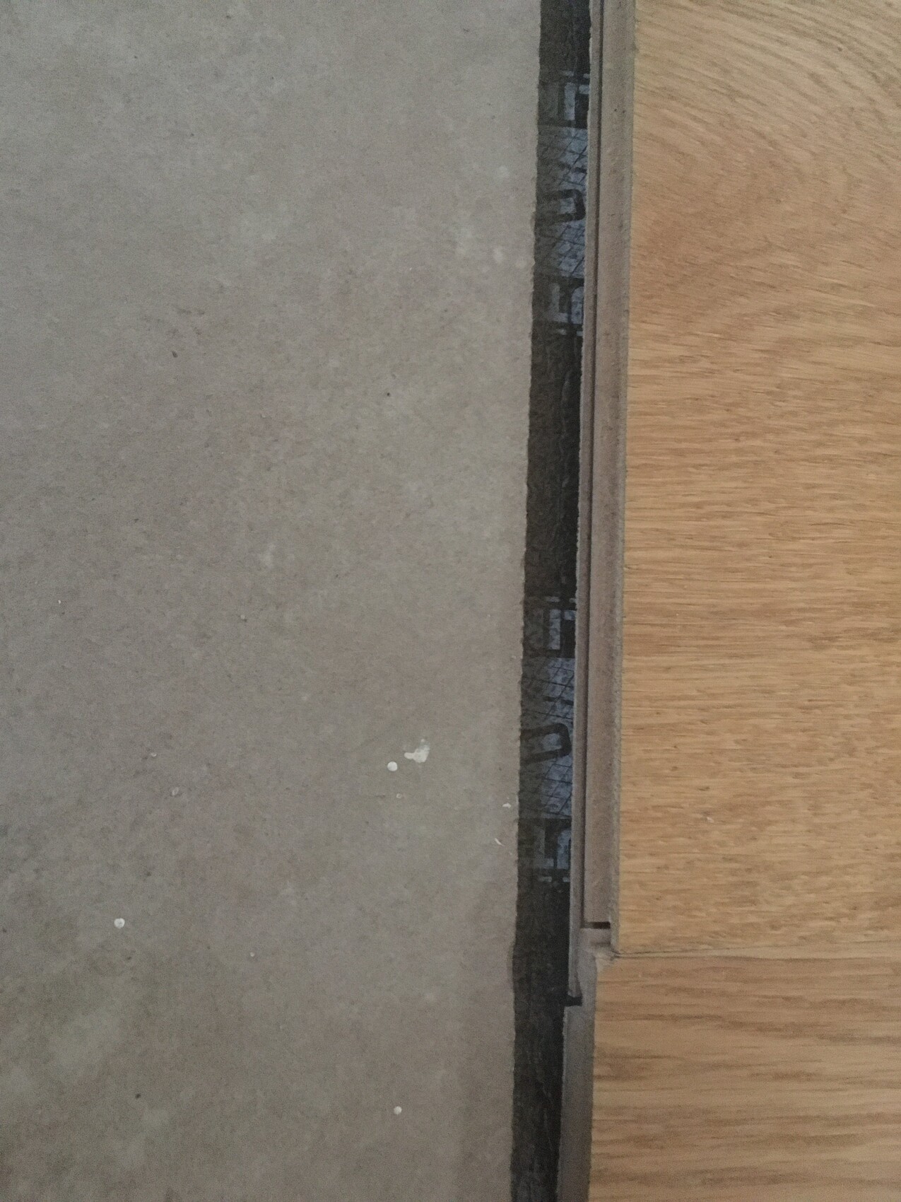 Türschwelle aus Metall zwischen grauem Betonboden links und Holzboden rechts.