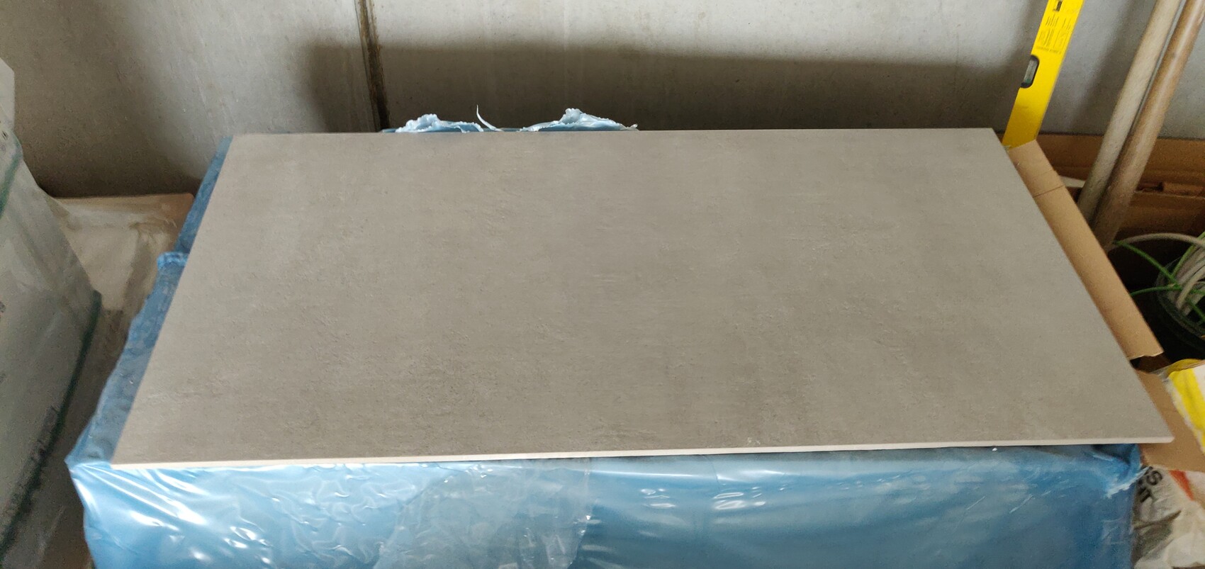 Große graue Fliesenplatte liegt flach auf blauem Schutzvlies in einer Werkstatt.