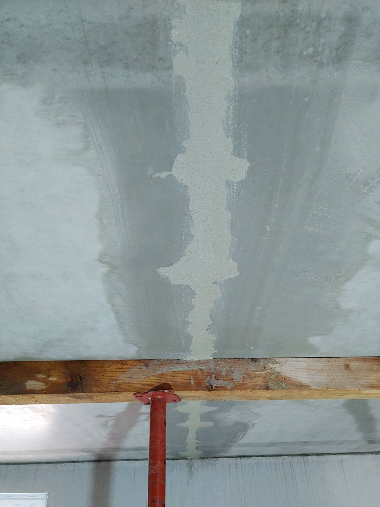 Baustellen-Decke mit senkrechter Putzfuge, rotem Stützpfosten und Holzbalken.