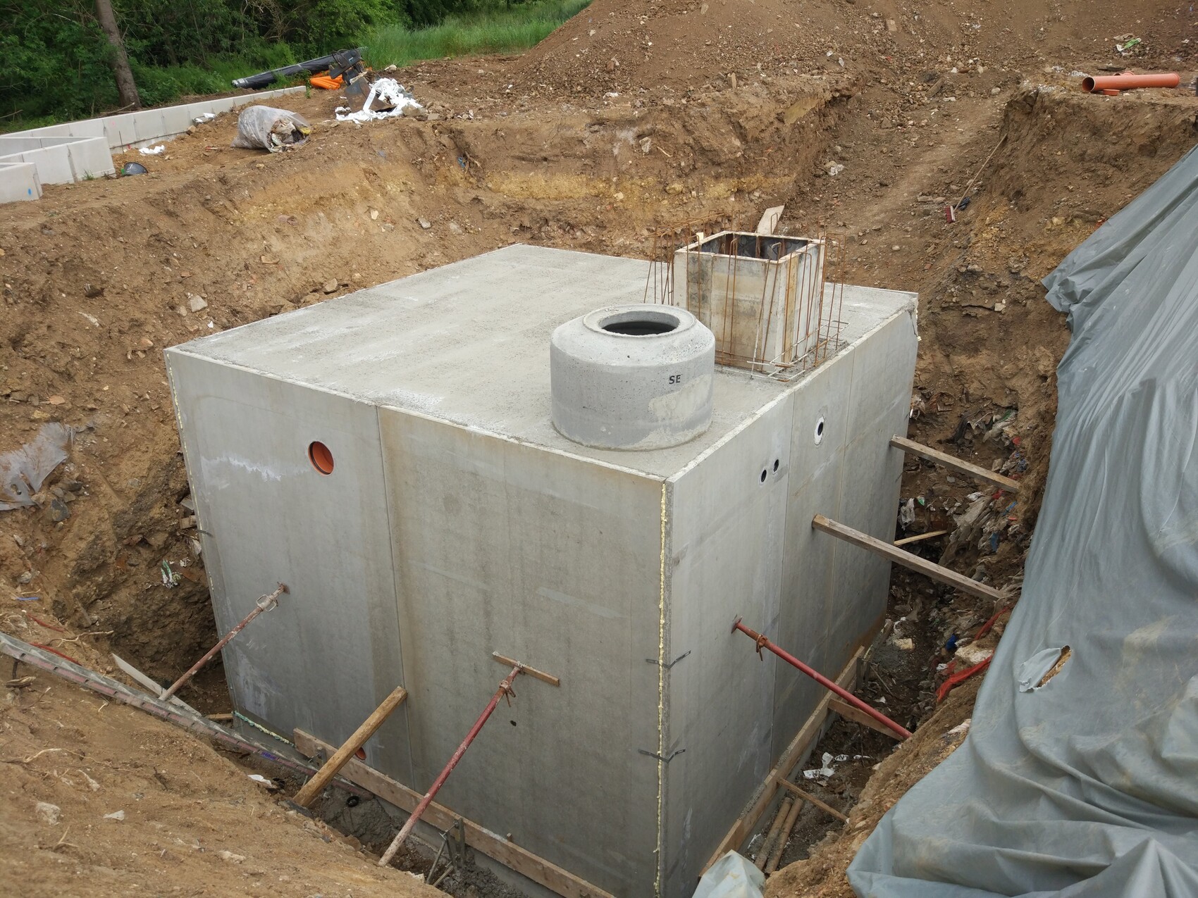 Großes Betonfundament in einer Baugrube mit runder Öffnung oben, Stahlbewehrung sichtbar, Holzstützen