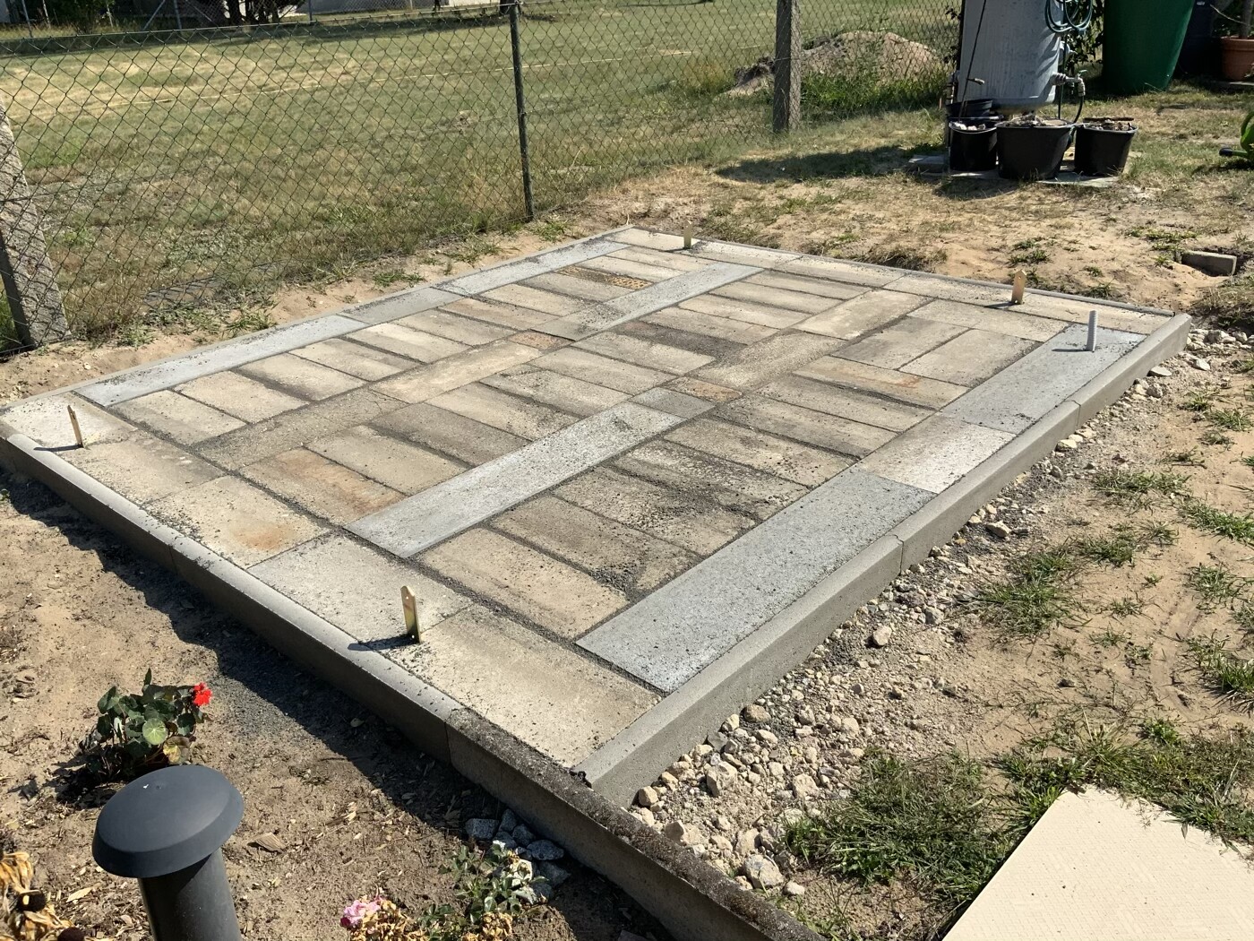 Neu verlegtes Pflaster-Patio aus rechteckigen Steinen mit Betonrand; Gartenzaun im Hintergrund.