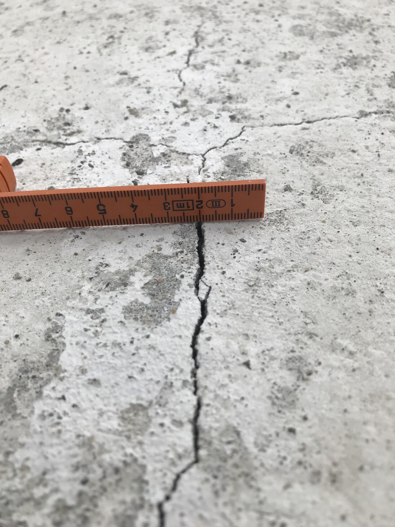 Riss in einer Betonplatte; ein orangenes Maßband misst die Breite des Risses.