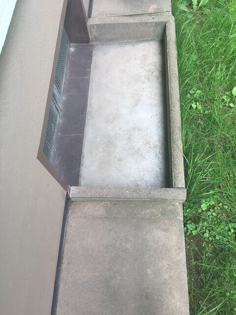 Außenbetonfundament mit Metallgitter neben Gras.