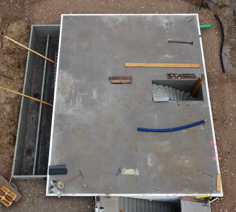 Draufsicht auf Baustellendecke: Metallplatte, offene Treppenöffnung, blauer Schlauch.