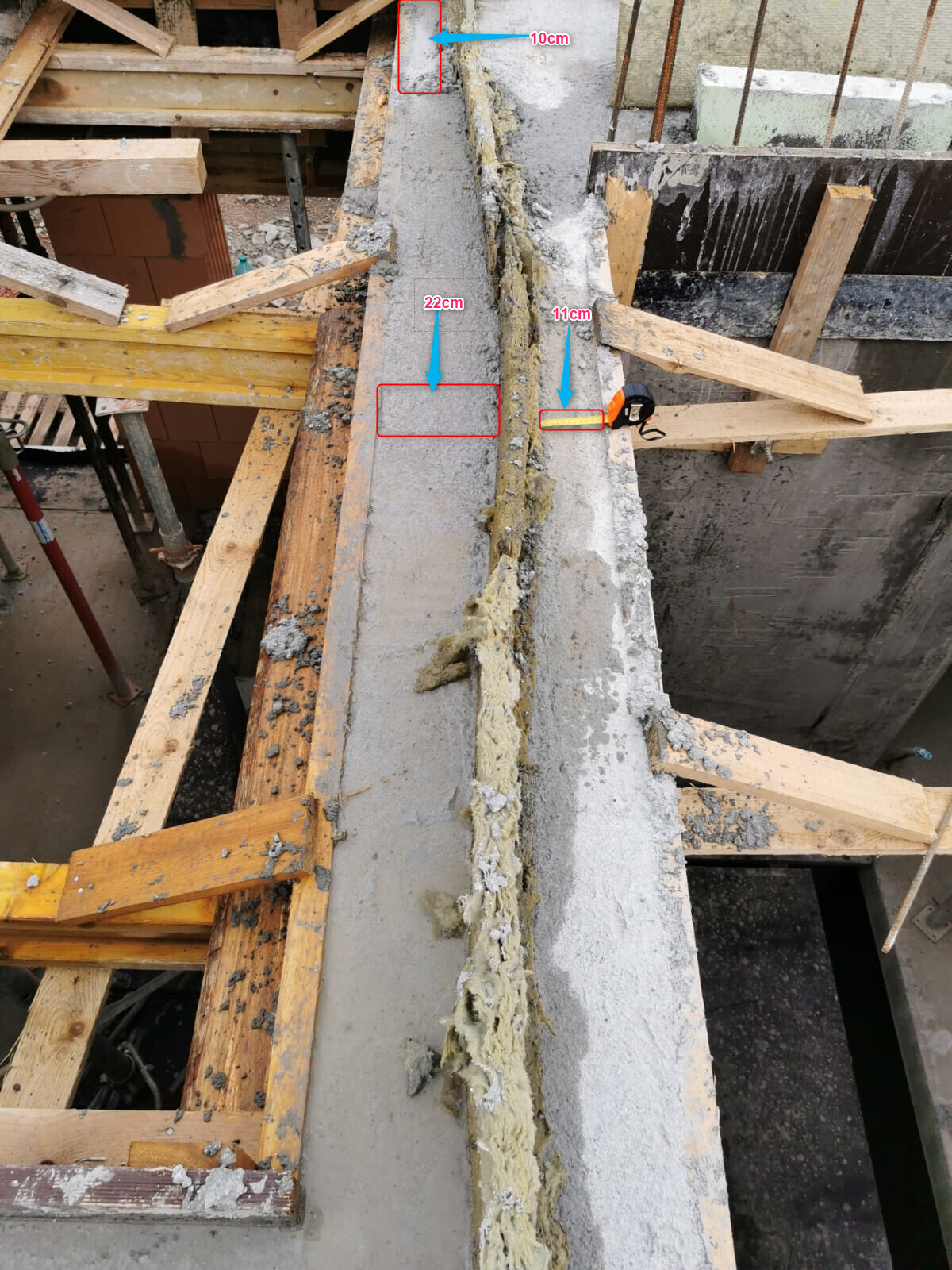 Baustelle: Betonbalken mit Fuge, Dichtmasse, Holzgerüst und Messmarken.