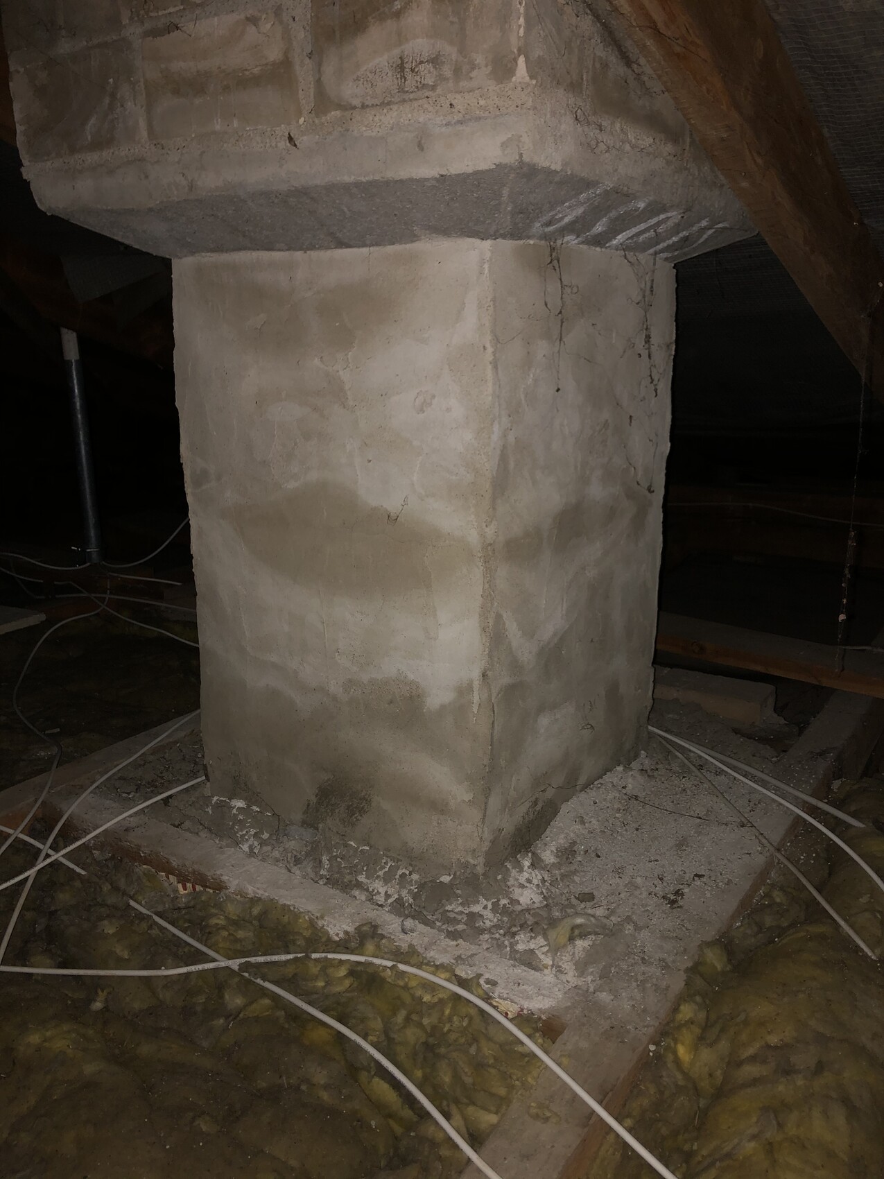 Betonpfeiler unter Holzbalkendecke; Kabel und Dämmmaterial liegen um den Pfeiler verstreut.