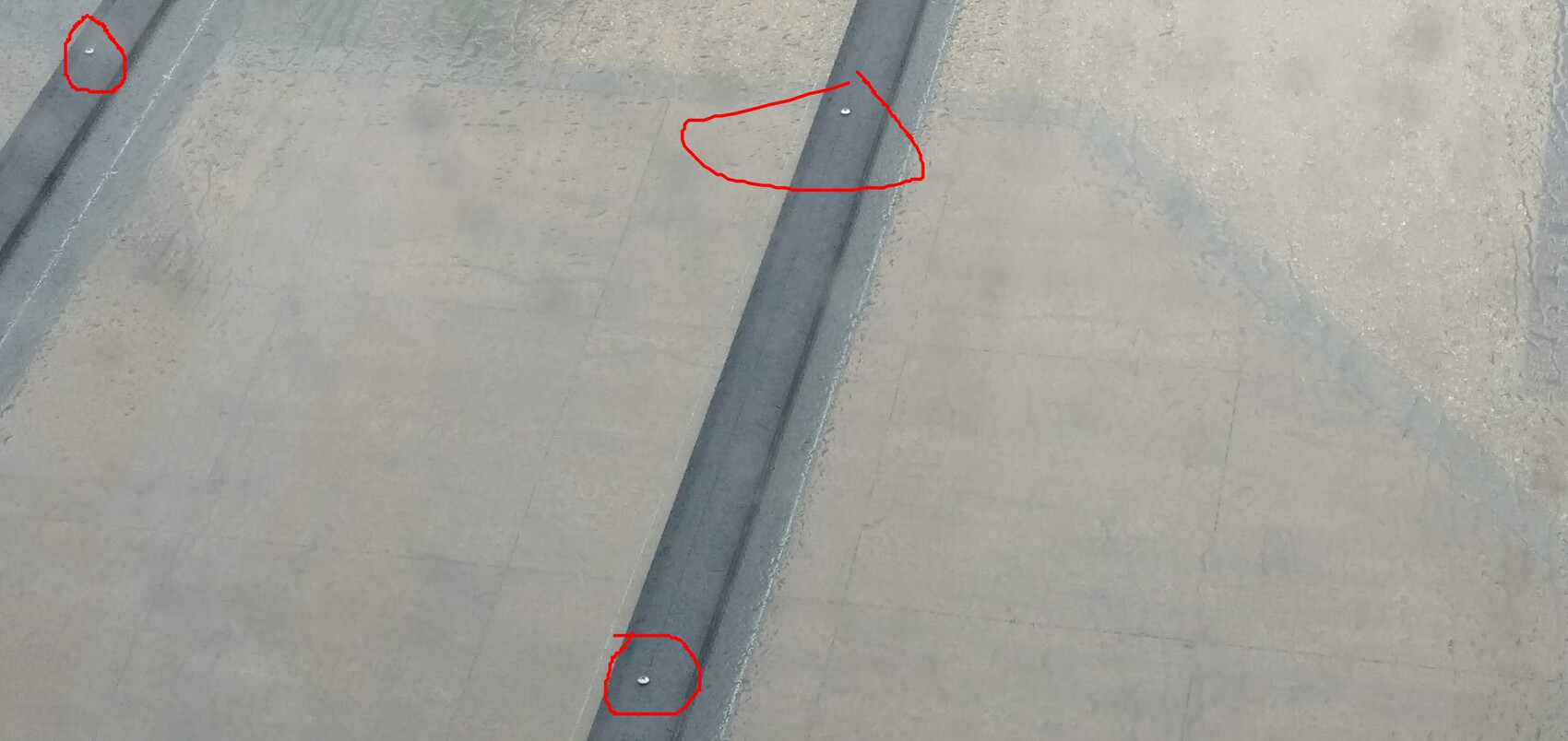 Draufsicht auf grauen Betonboden mit dunkler Fuge; drei silberne Schrauben.