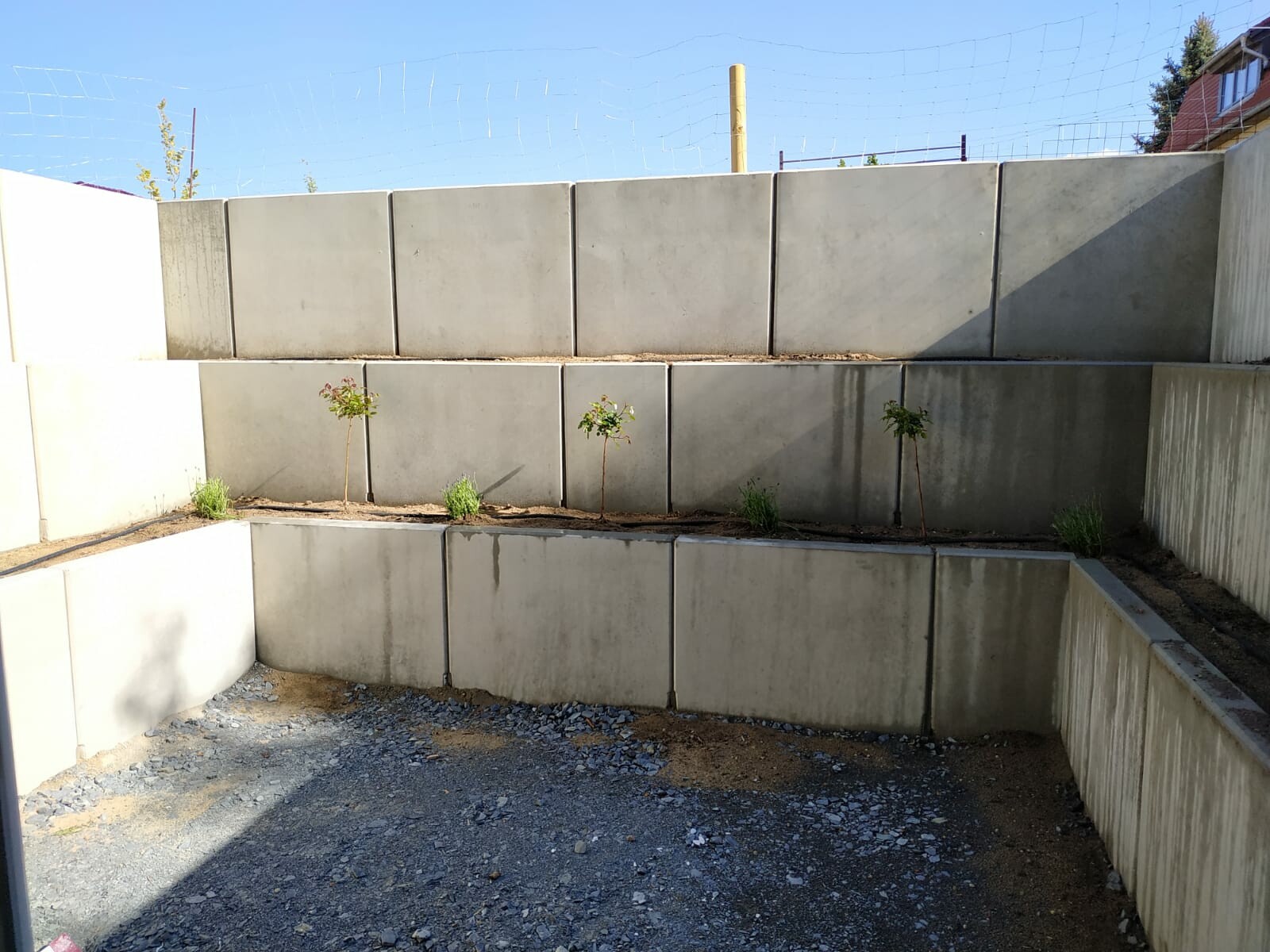 Mehrstufige Betonmauer aus großen Quadern mit kleinen Bäumen und Gräsern in Beetflächen