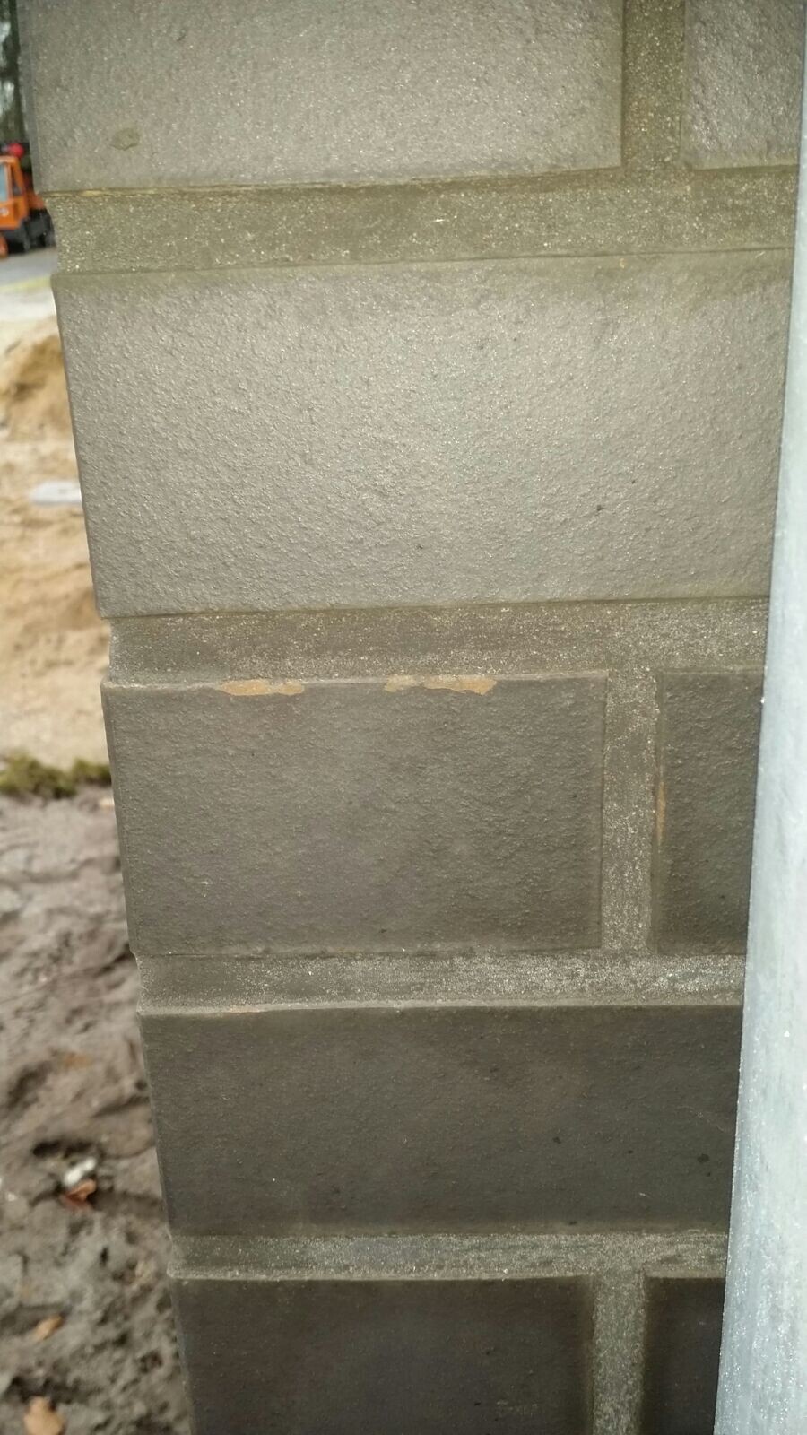 Nahaufnahme einer Außenwand aus Betonblocksteinen im Rohbau, Baustelle im Hintergrund