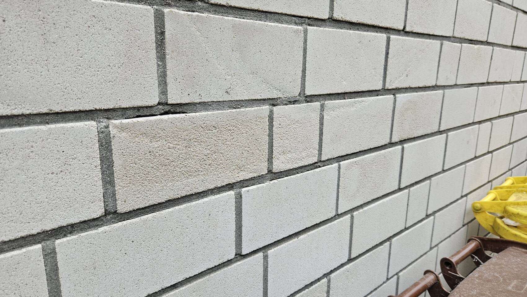 Graue Betonblockwand mit deutlichen Fugen; unten rechts gelbe Bauausrüstung.