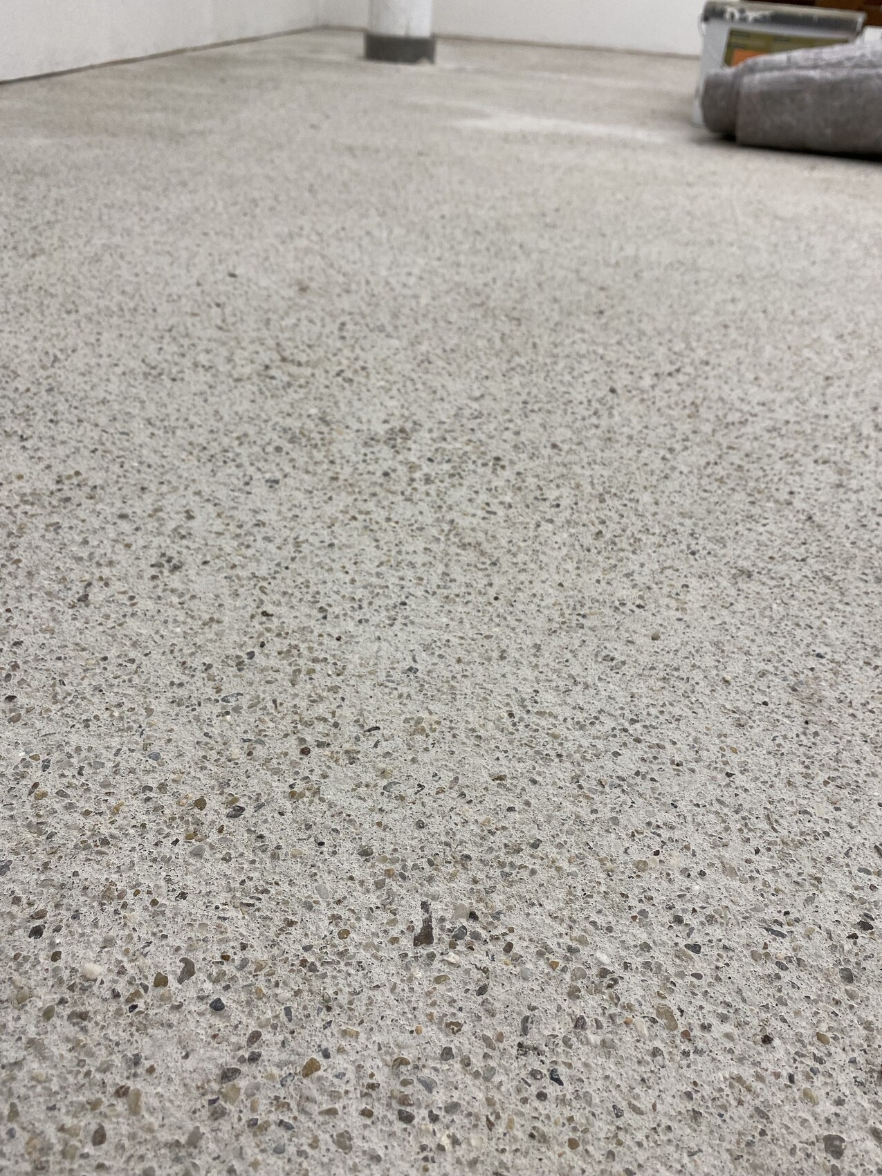 Grob gemusterter Beton-/Terrazzo-Boden in Innenraum; Farbeimer und Farbrolle liegen oben rechts.