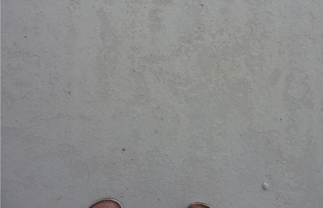 Blick von oben auf rauen hellgrauen Betonboden mit roten Schuhspitzen am unteren Rand.
