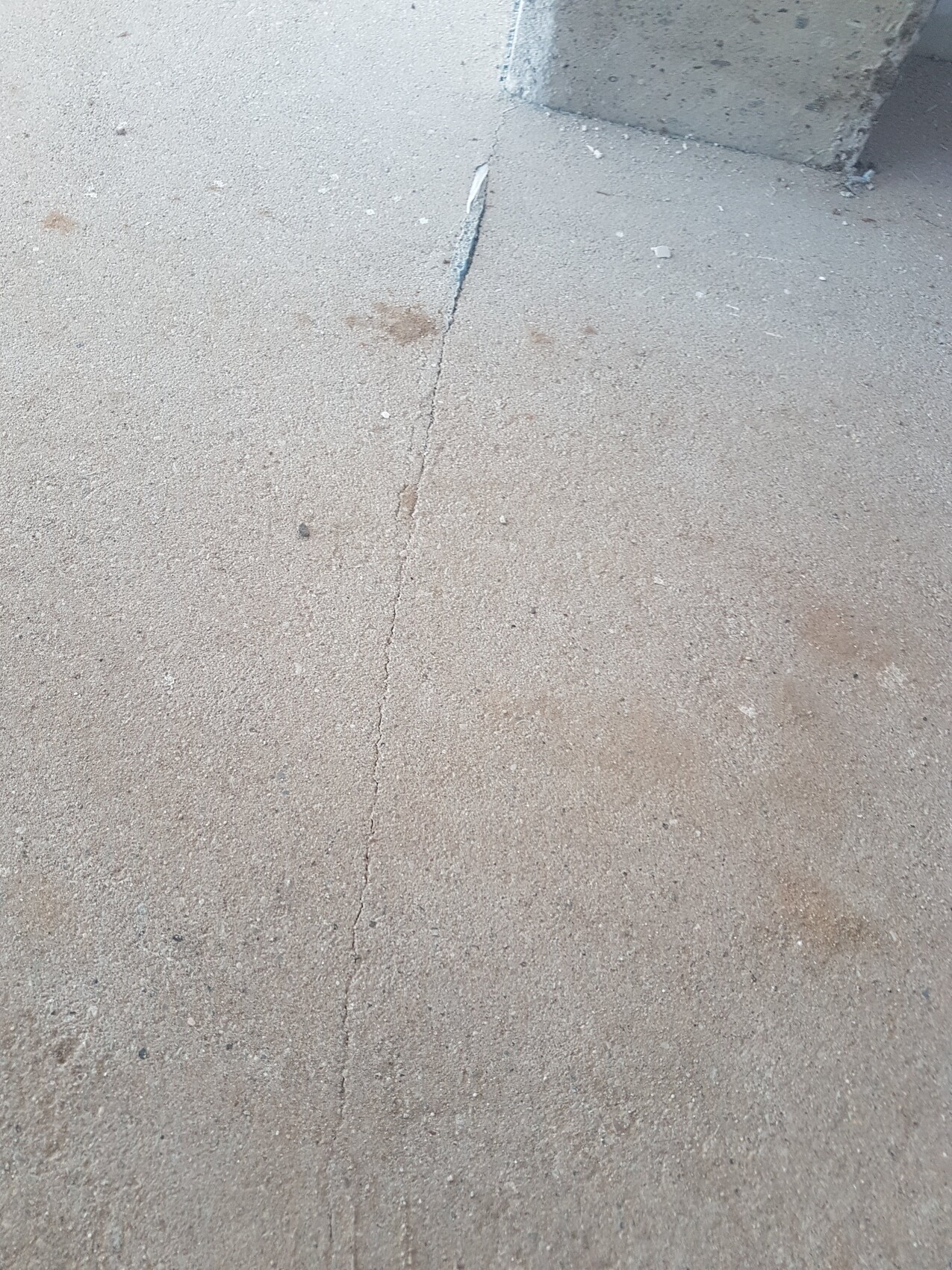 Betonboden mit feiner Vertikalrisslinie, staubig, Ecke einer Betonwand oben rechts sichtbar.