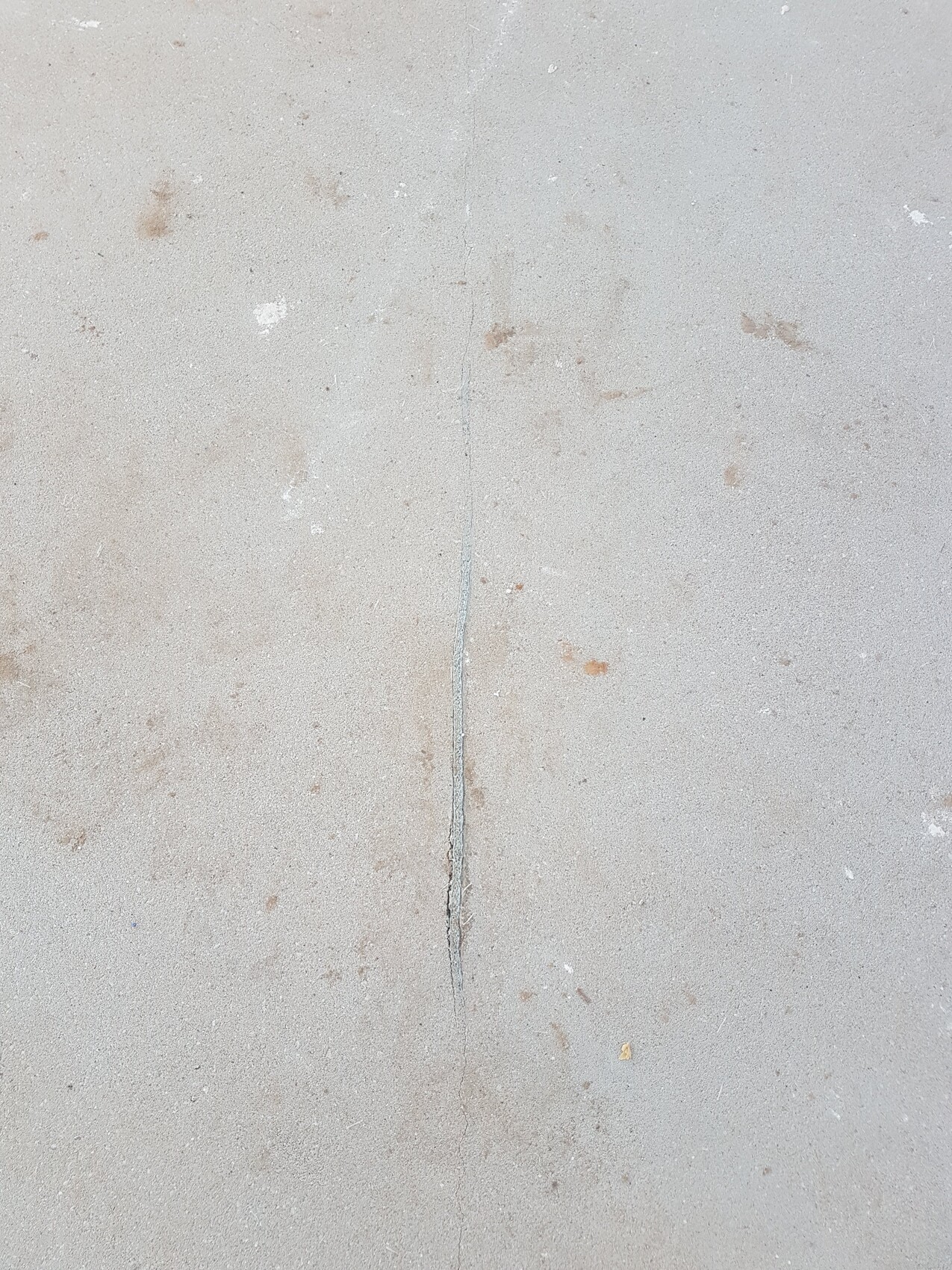 Graue Betonoberfläche mit einer senkrechten Risslinie in der Mitte.