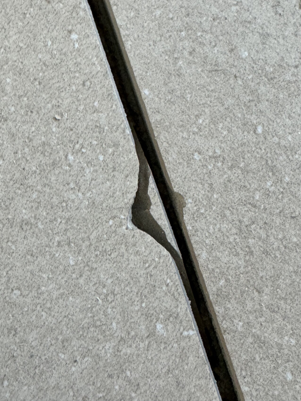 Diagonaler Riss in einer hellgrauen Betonoberfläche, dunkler Spalt entlang der Fuge.