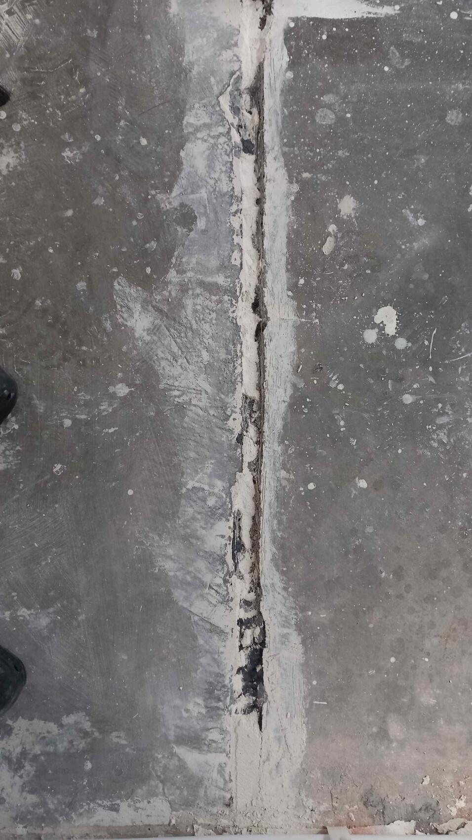 Betonboden mit vertikalem Riss in der Mitte, umgeben von Dichtmasse.