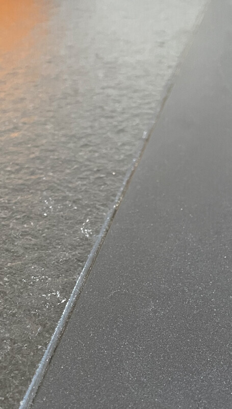 Nahaufnahme einer Kante: raue Steinoberfläche links, glatte dunkle Platte rechts.