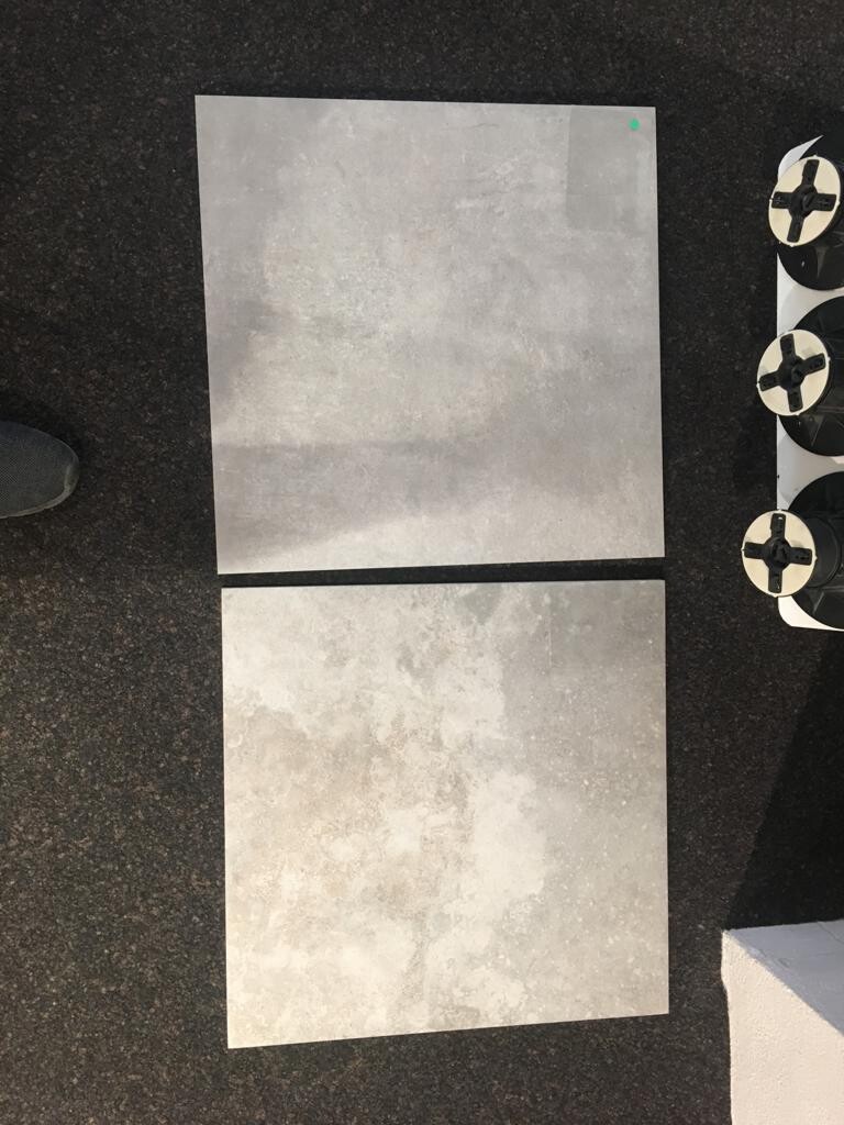 Zwei graue Betonfliesen liegen auf Asphalt, rechts Ventilatoren, links Fuß sichtbar.