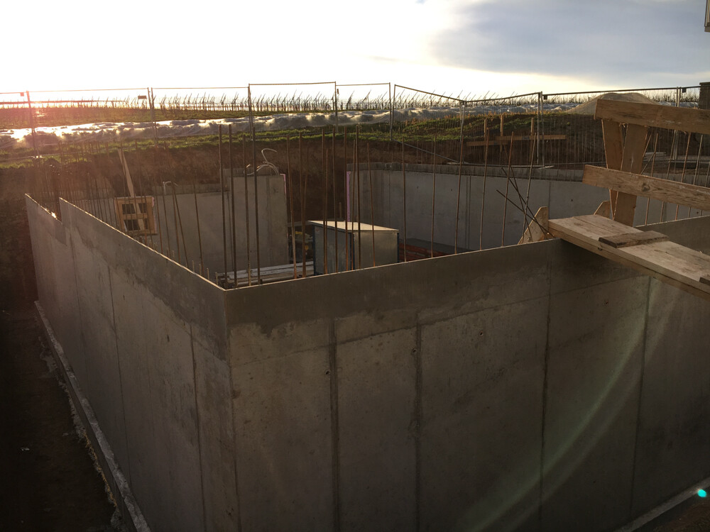 Betonfundament mit Stahlbewehrung, Holzformteile und Abendsonne über der Baugrube.