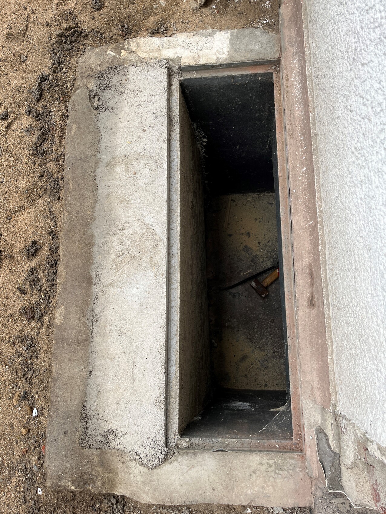 Offener Betonschacht am Haus, dunkler Innenraum, rechteckige Form, Erdreich drumherum.