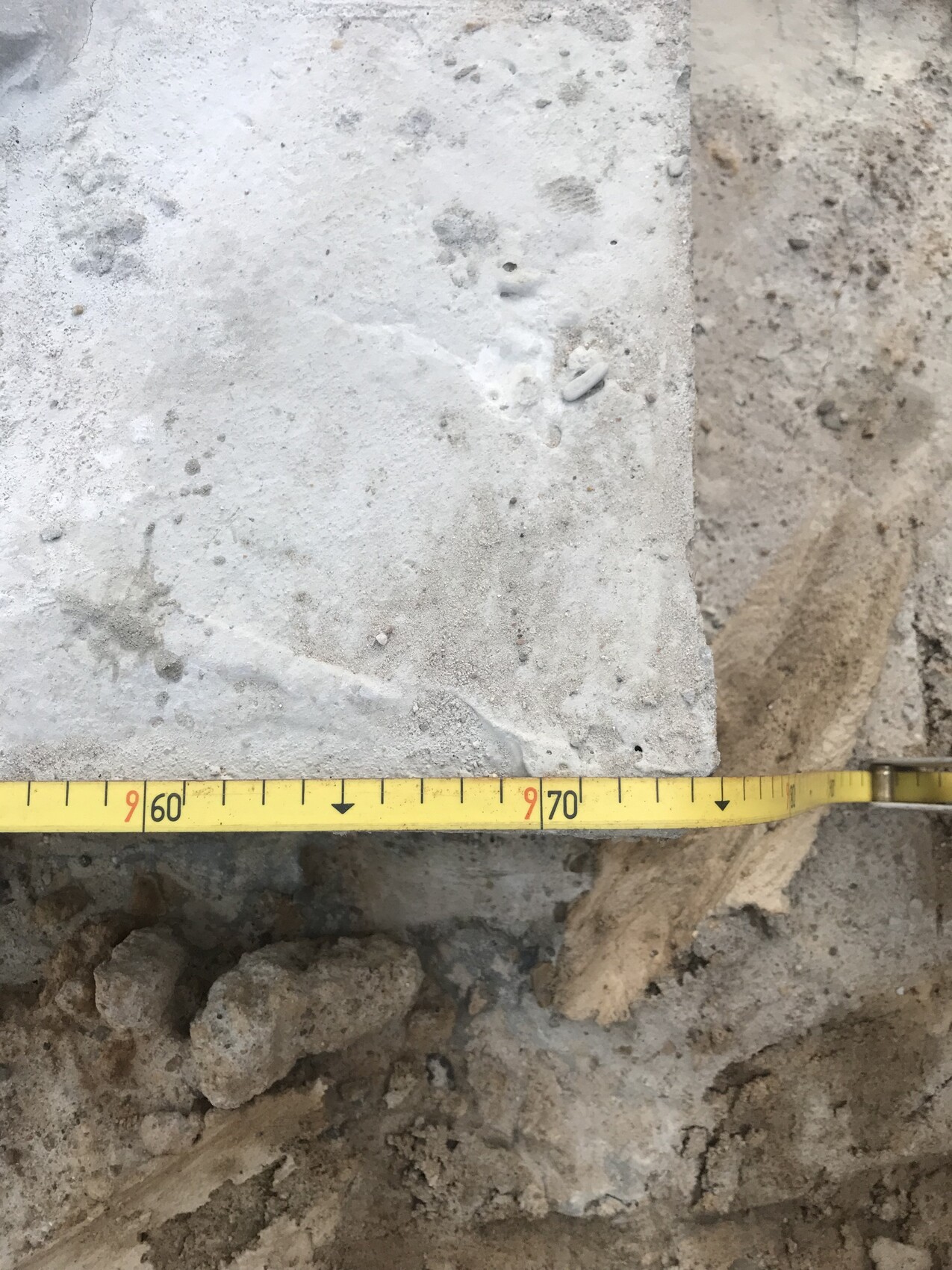 Gelbes Maßband liegt quer über eine Betonplatte auf einer Baustelle, ca. 60–70 cm ablesbar.