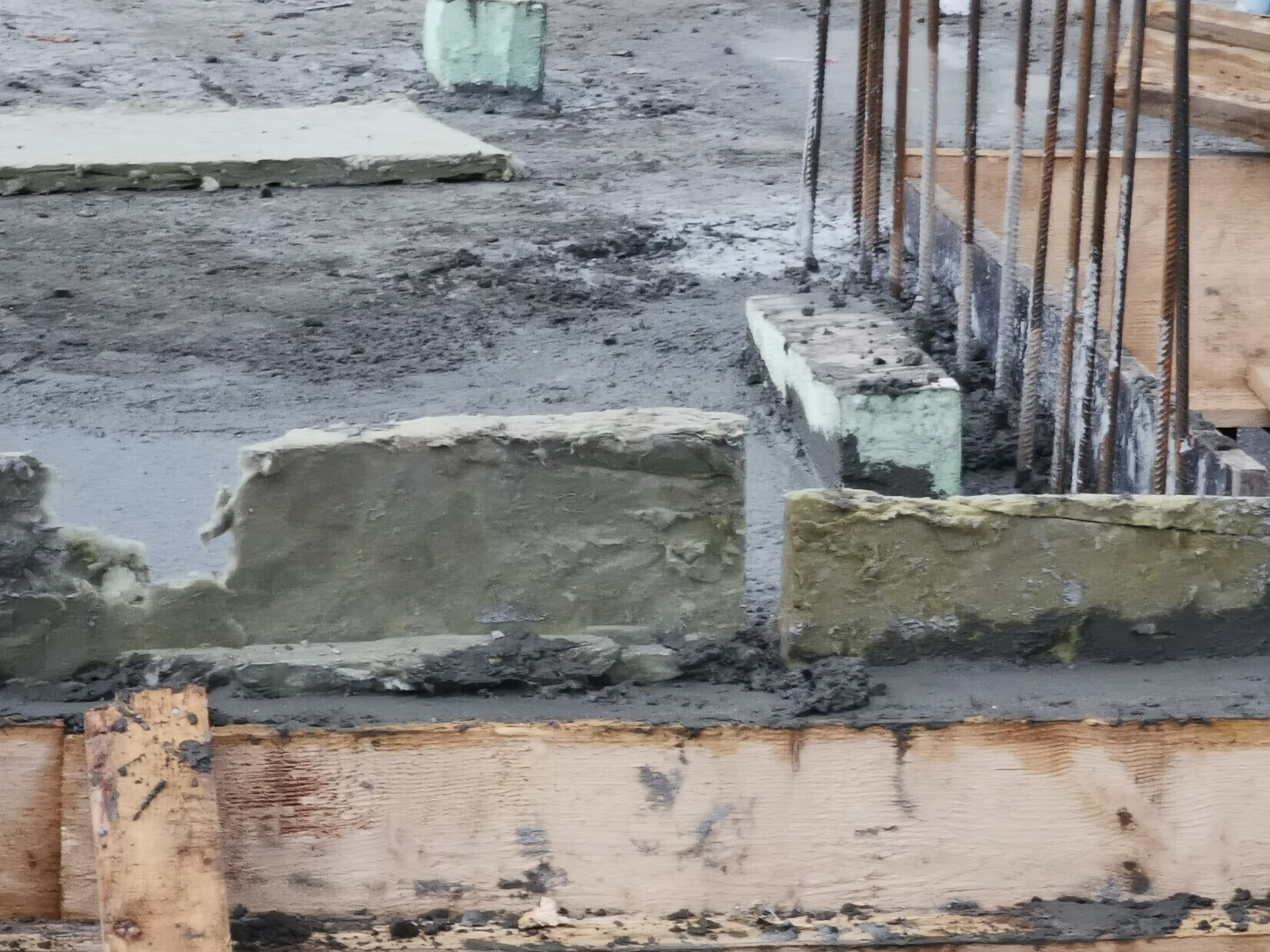Frischbetonfundament mit Stahlbewehrung und Holzformen in einer Baugrube.