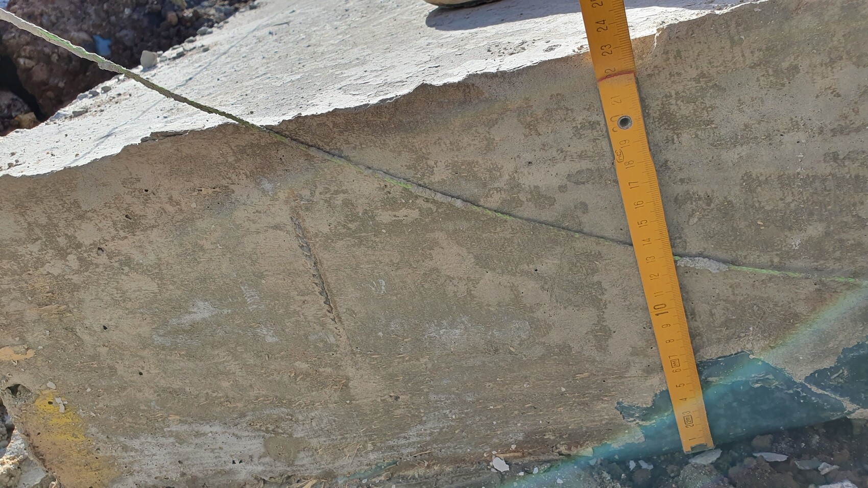 Grobe Betonoberfläche mit diagonalem Riss; daneben liegt ein gelbes Messband.