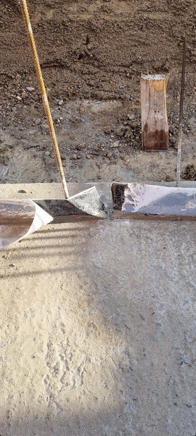 Baustelle: roher Betonboden, Holzpfosten, Seil, Bewehrungsstahl und Kies.