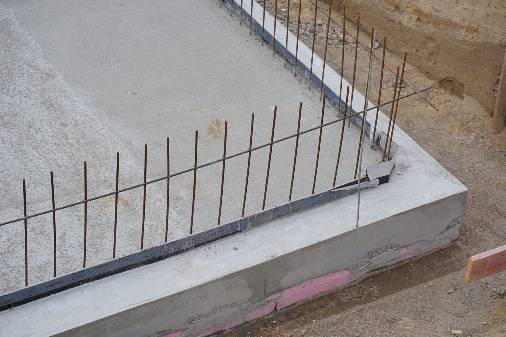 Baustelle: Rostige Bewehrungsstangen ragen aus einer frischen Betonfundamentplatte.