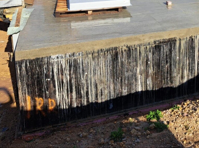 Betonblock mit abtropfendem Wasser an der Seite und orange Markierung 12D auf einer Baustelle.