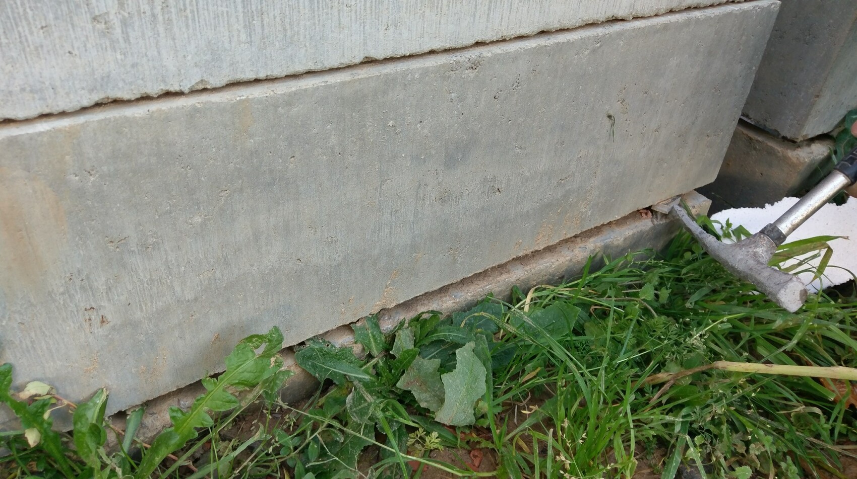 Nahaufnahme eines Betonfundaments mit Gras am Sockel und Bauteilen