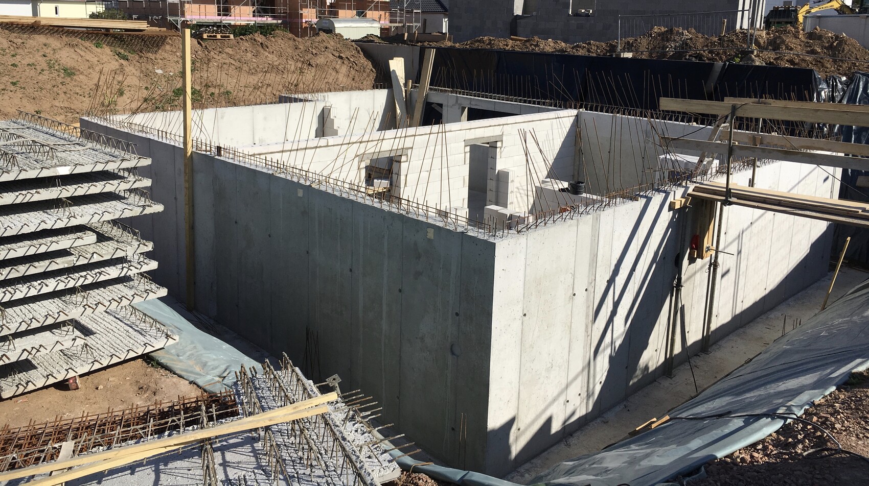 Betonfundament mit Stahlbewehrung in Baugrube; Rohbau der zukünftigen Wände entsteht.
