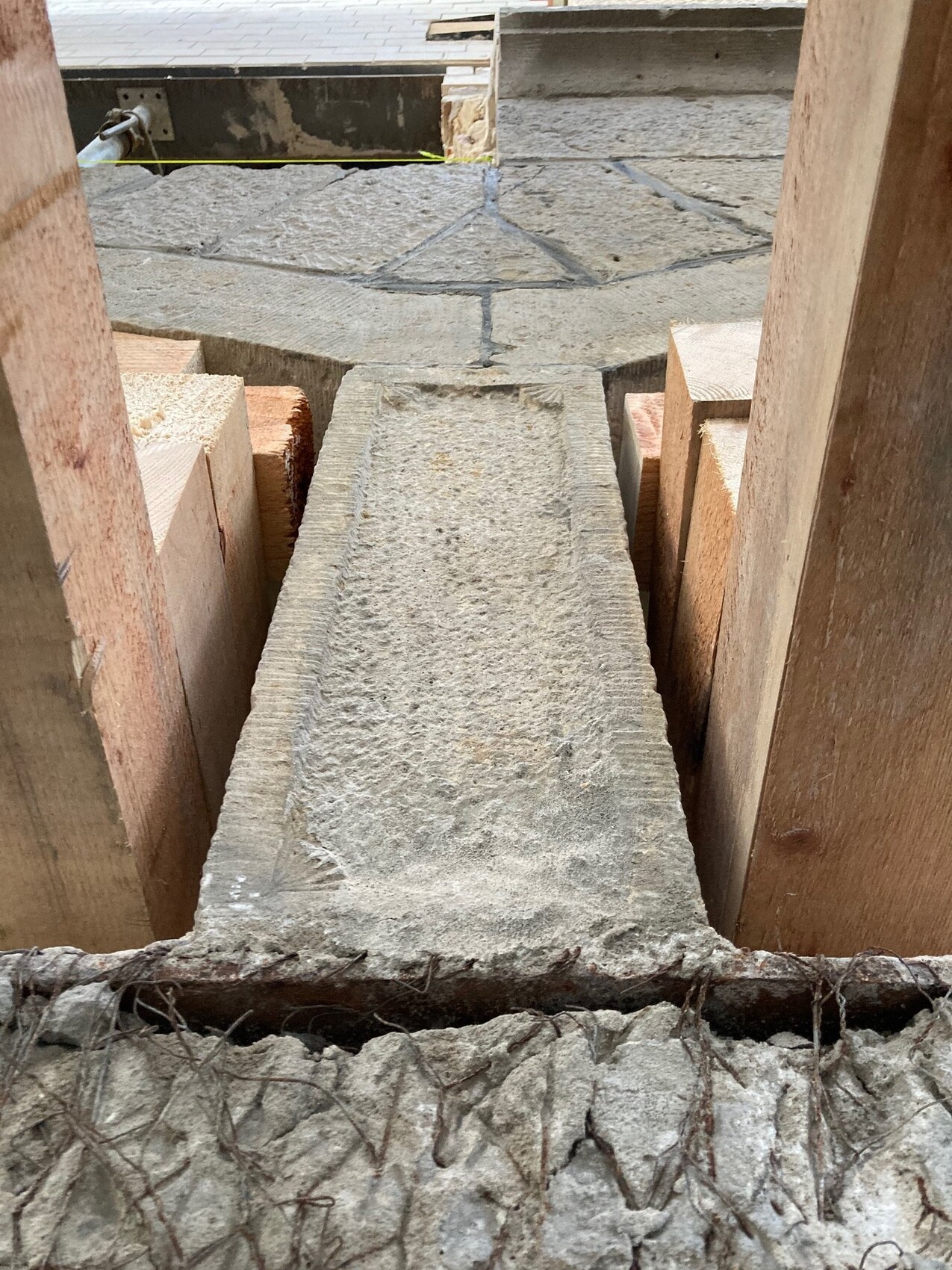 Baustelle: Eine lange grobe Betonplatte liegt zwischen Holzformen, unten Drahtbewehrung sichtbar.
