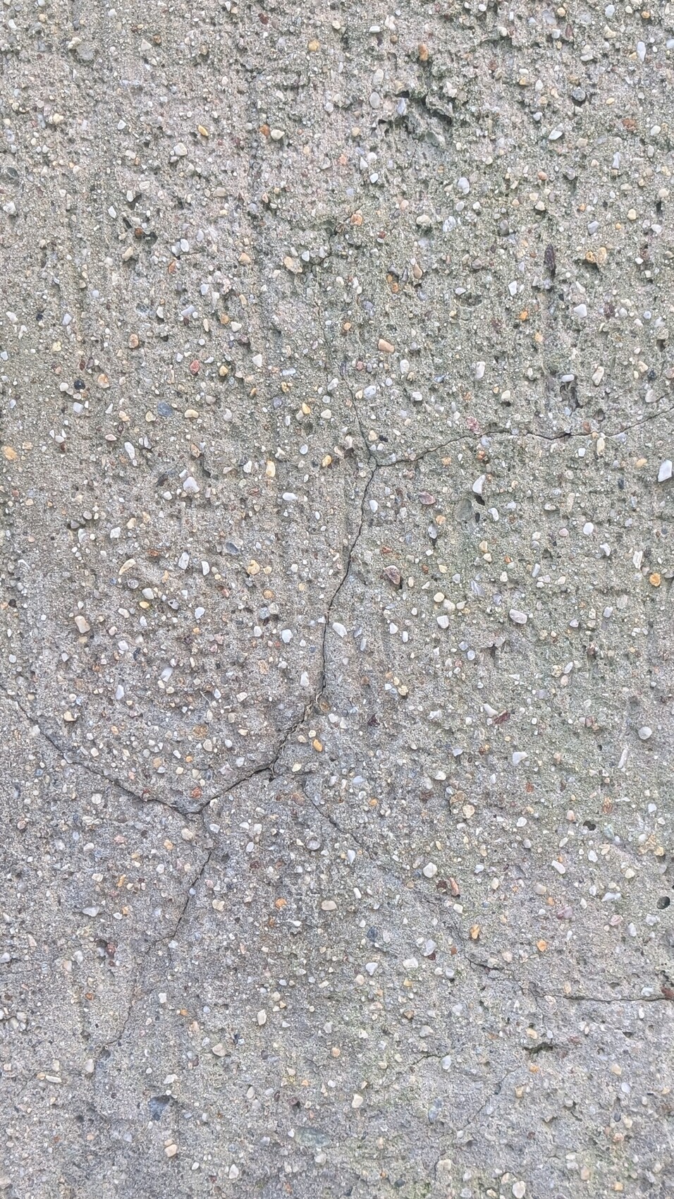 Raues Betonoberfläche mit Kieseln und sichtbaren Rissen.