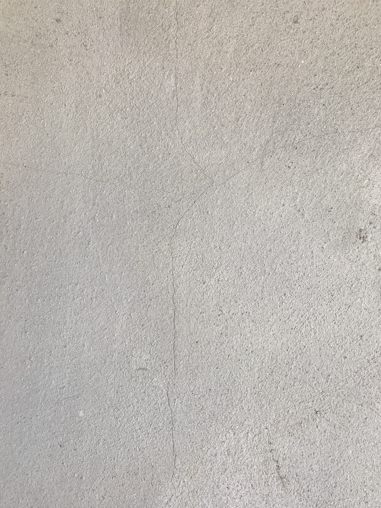 Nahaufnahme einer grauen Betonoberfläche mit Rissen und leichter Körnung.