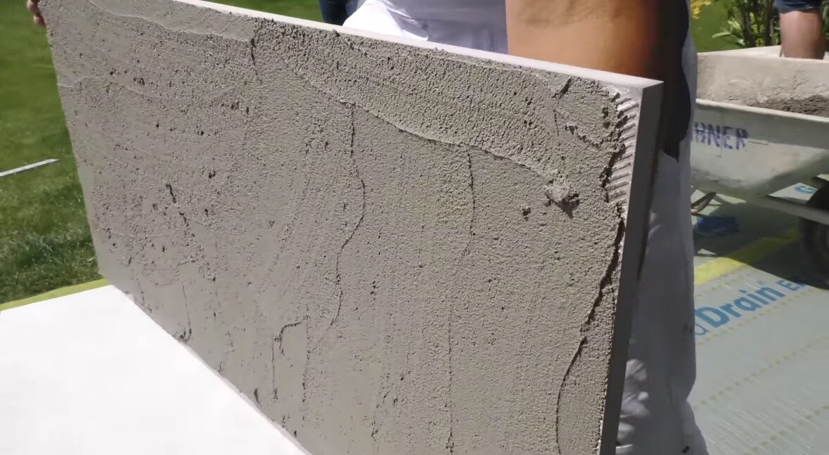 Große Betonplatte mit Rissen wird von Händen gehalten, Bauumgebung im Hintergrund.