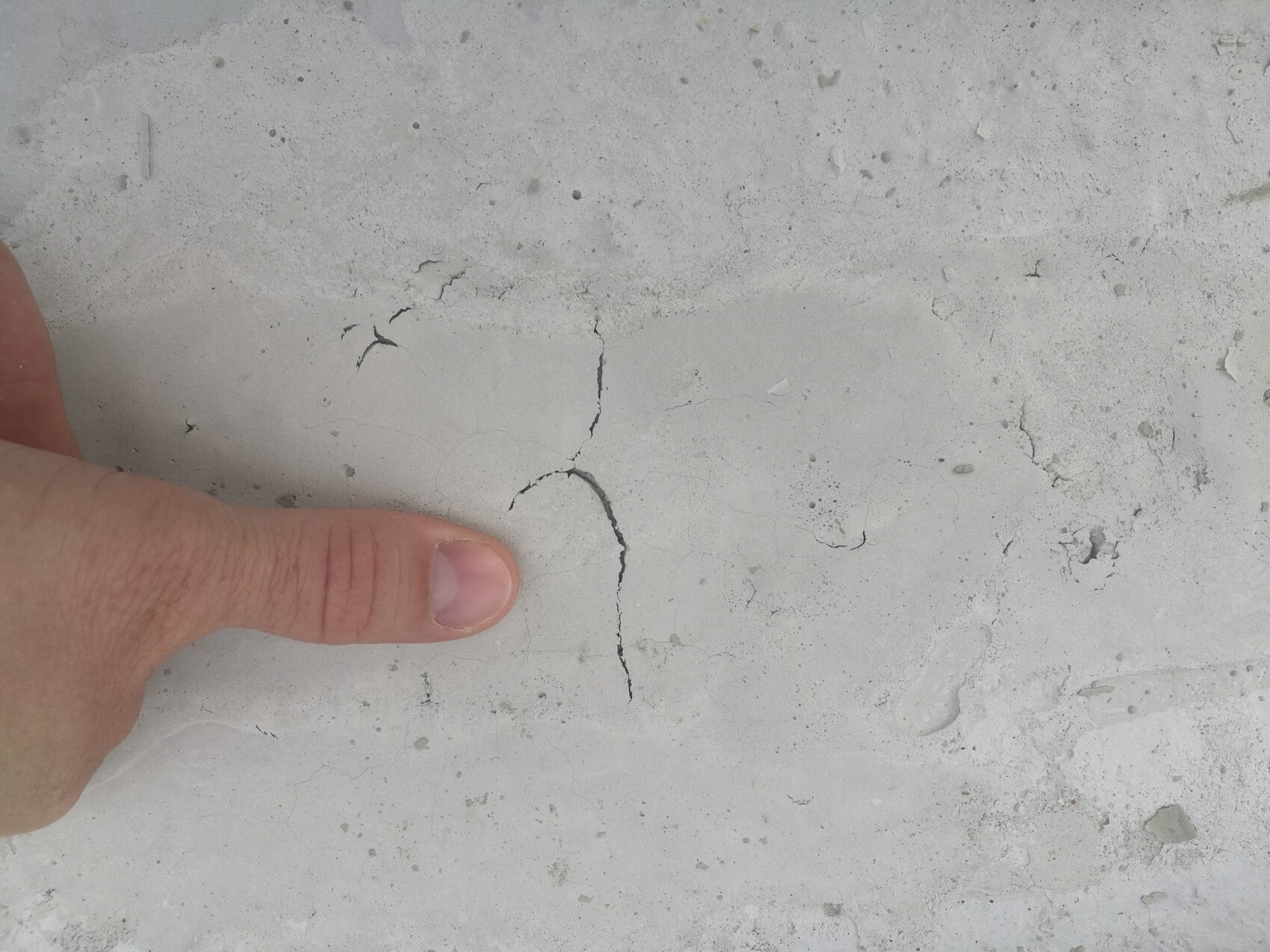 Finger zeigt Risse in grauem Betonboden, Hinweis auf Baumangel im Bau