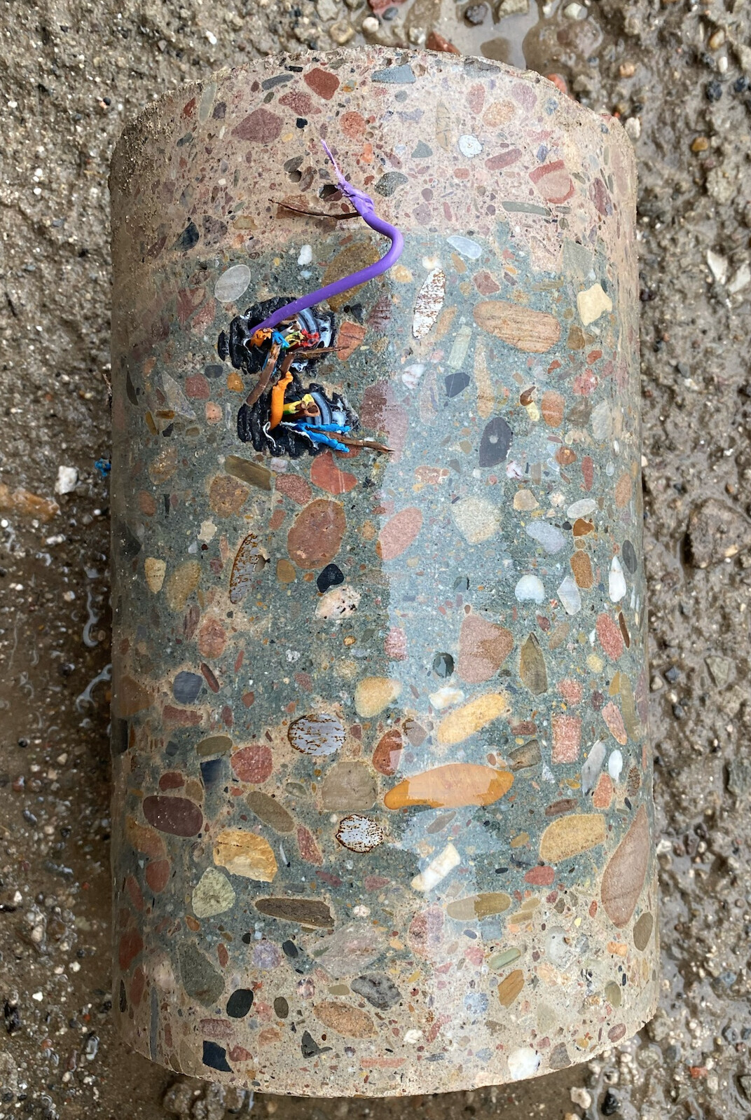 Zerbrochene Betonröhre mit Terrazzo-Einlagen und freiliegenden bunten Kabeln.