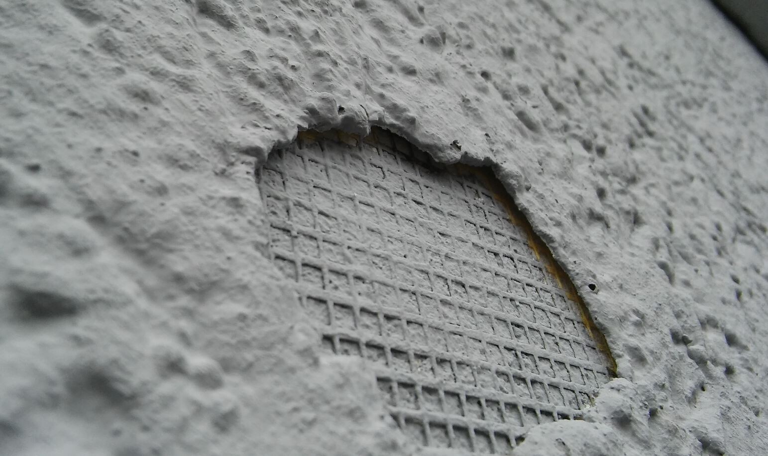 Nahaufnahme einer rauen Betonwand mit rundem Loch und Bewehrungsnetz dahinter