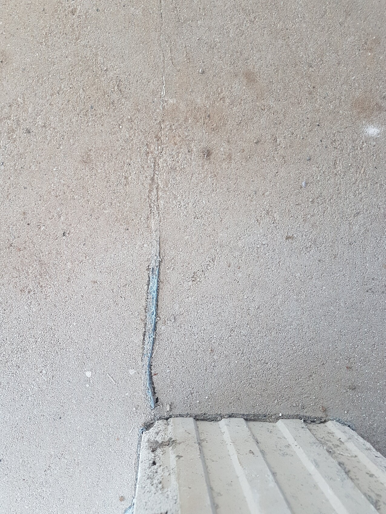Vertikaler Riss in einer rauen Betonwand, daneben eine Treppenstufe sichtbar.