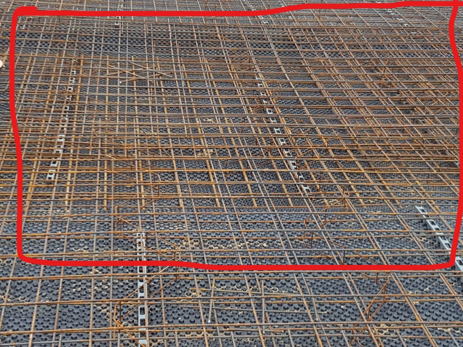 Auf einer Baustelle liegt ein rostiges Bewehrungsnetz aus Stahlstangen.