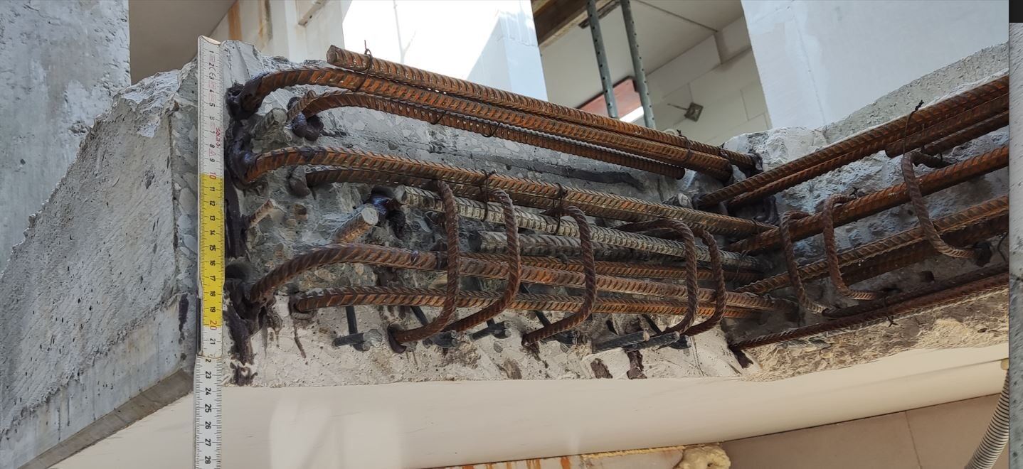 Rostige Bewehrungsstähle ragen aus Beton, Messband zeigt Maße an einer Baustelle.